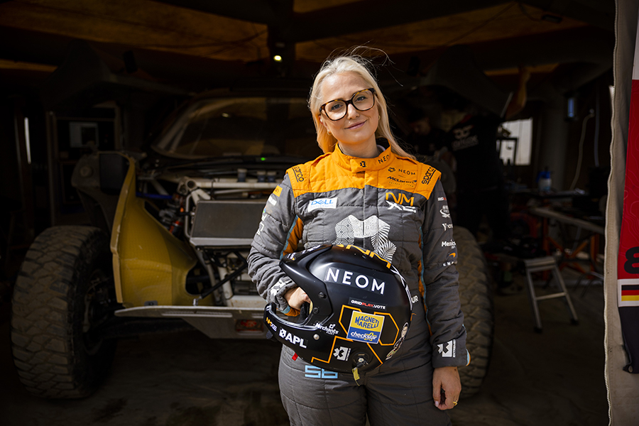 Tamara Molinaro with helmet in hand in front of the garage of her 2023 Extreme E SUV